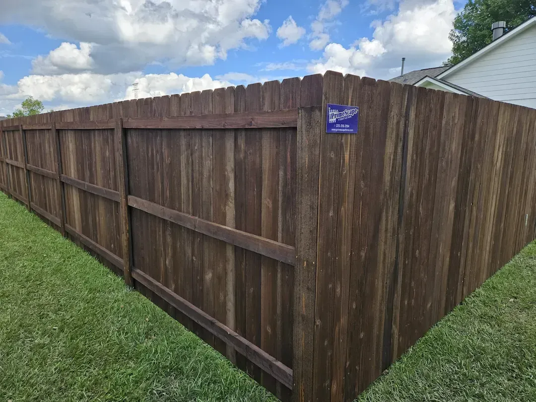 Long wooden privacy fence along a grassy yard under a cloudy blue sky