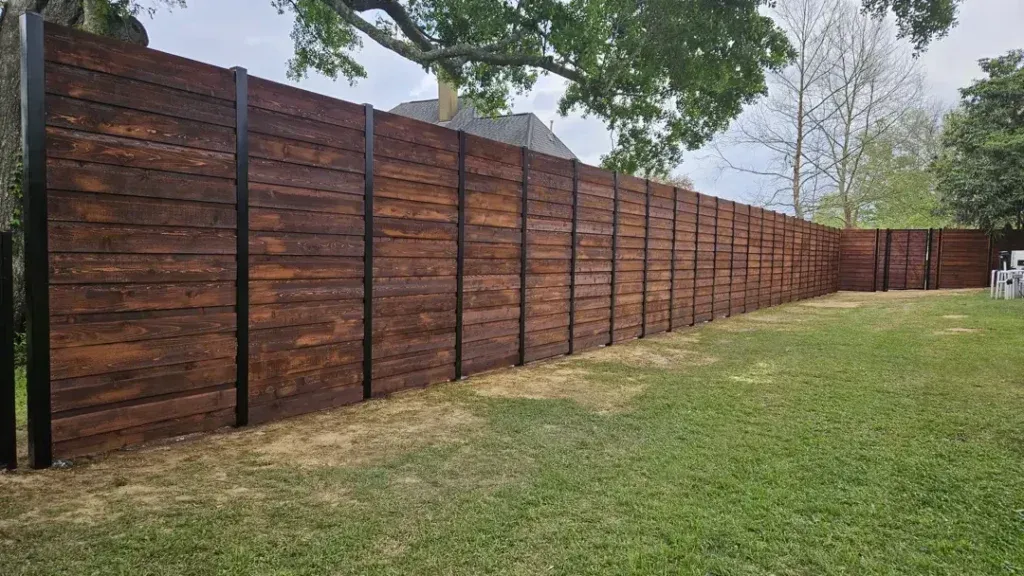 Wooden privacy fence with black posts enclosing a yard beside grass and trees