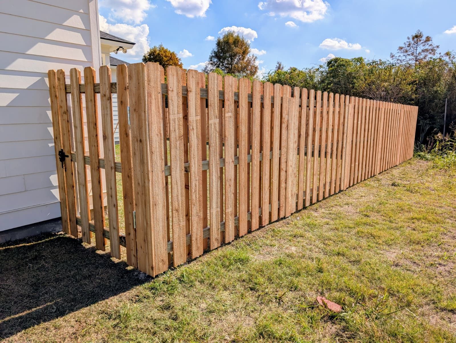 Long wooden fence beside a white house on a grassy yard