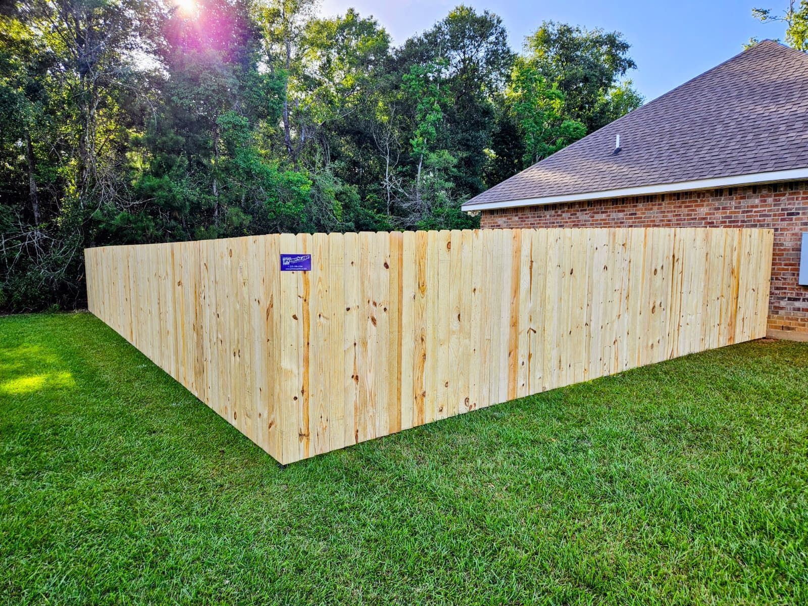 Wooden privacy fence enclosing a yard beside a brick house on a green lawn.