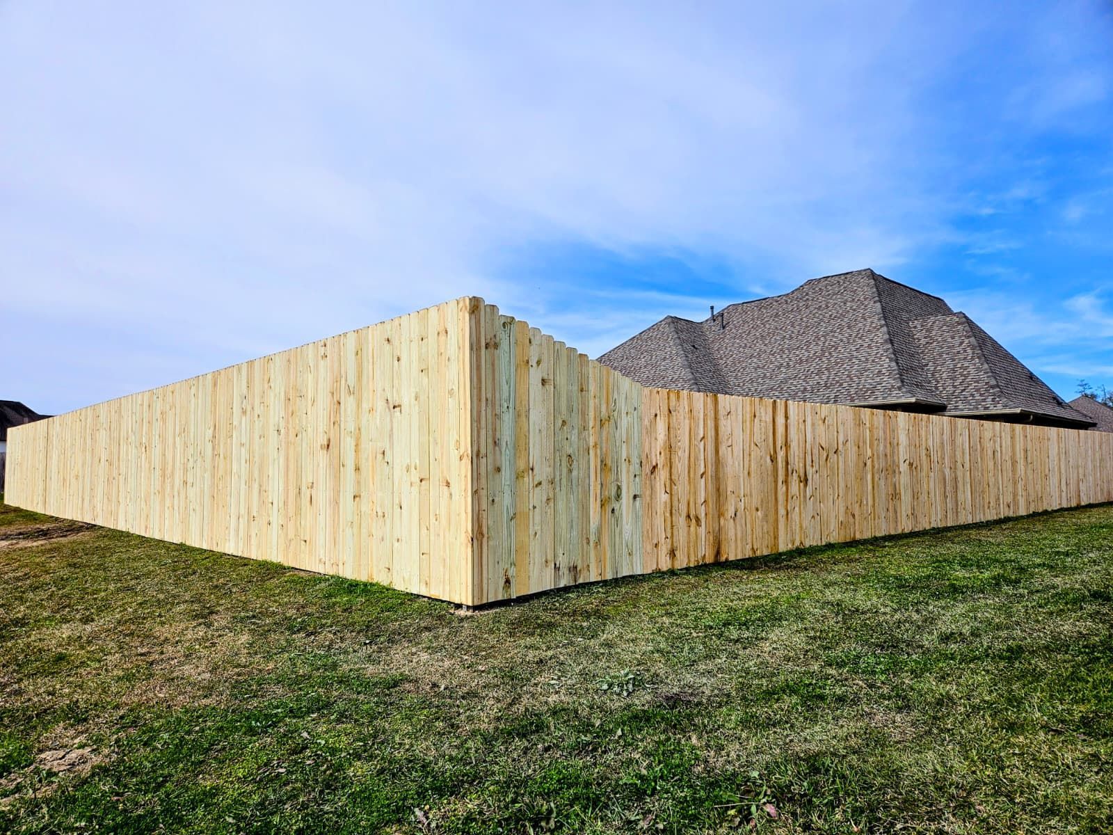 Wooden privacy fence surrounding a yard under a blue sky, with a house roof visible behind it.