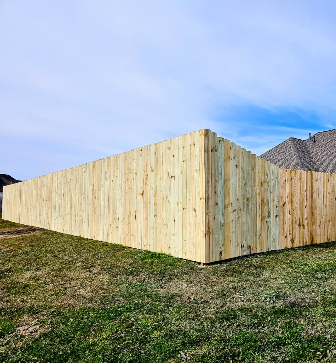 Wooden privacy fence around a yard with a house roof visible behind it under a blue sky