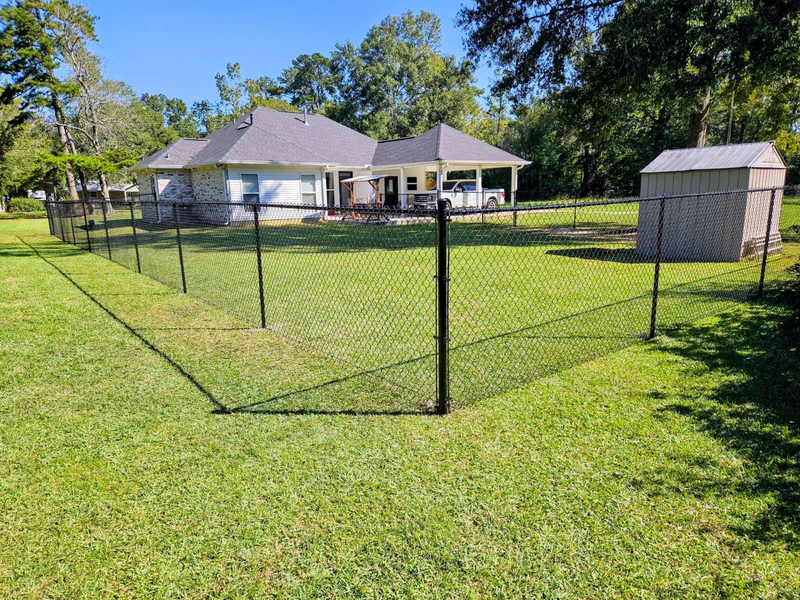 Backyard with a chain-link fenced area, a house, and a small shed on a sunny day