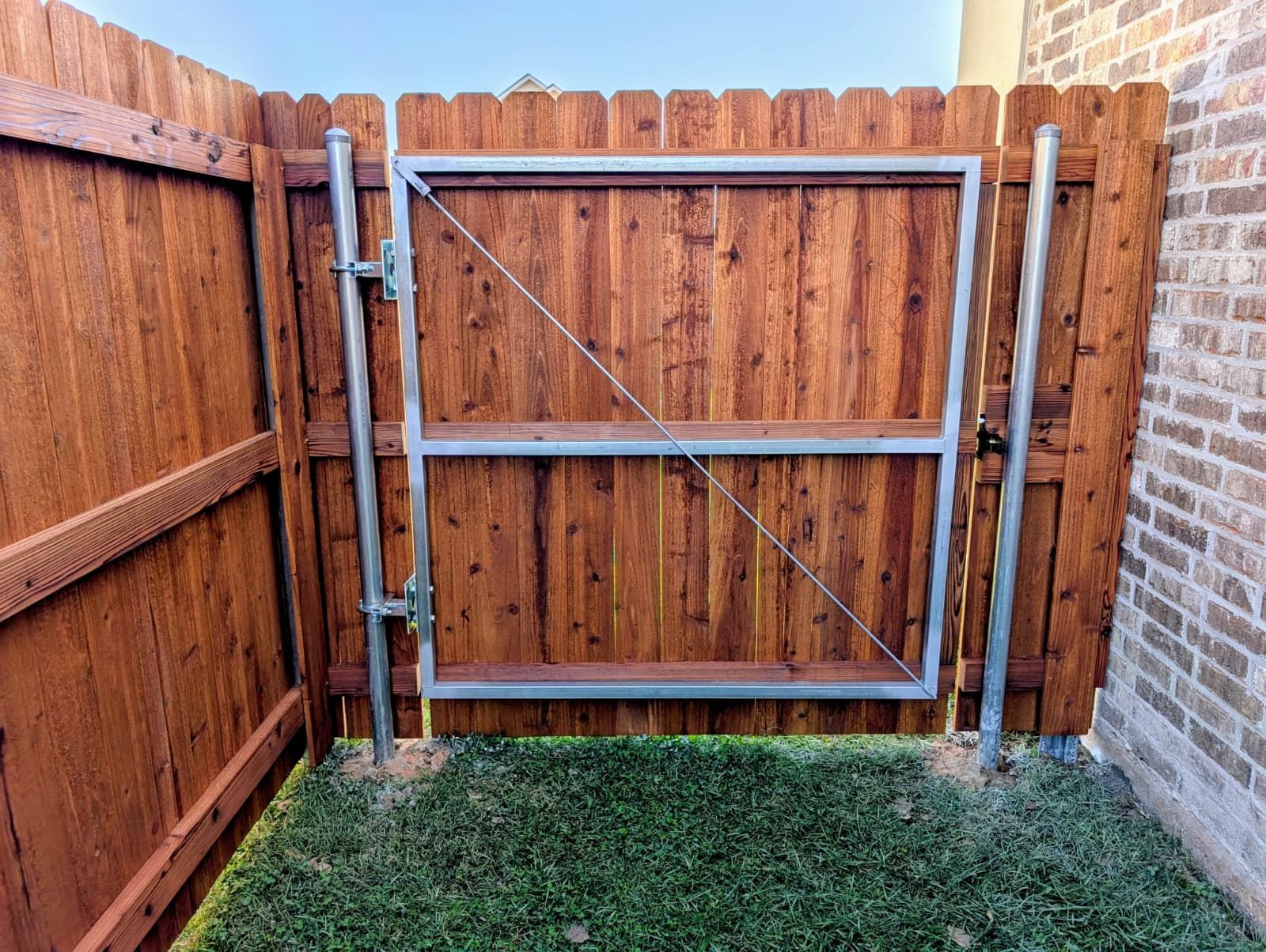 Wooden backyard gate set in a fence beside a brick wall with grass below
