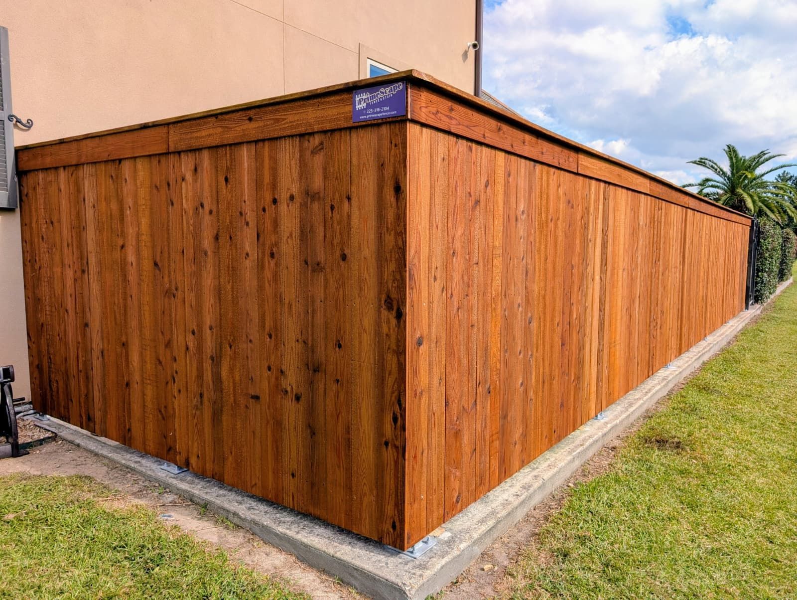 Wooden privacy fence with a slanted top beside a beige building and grassy yard