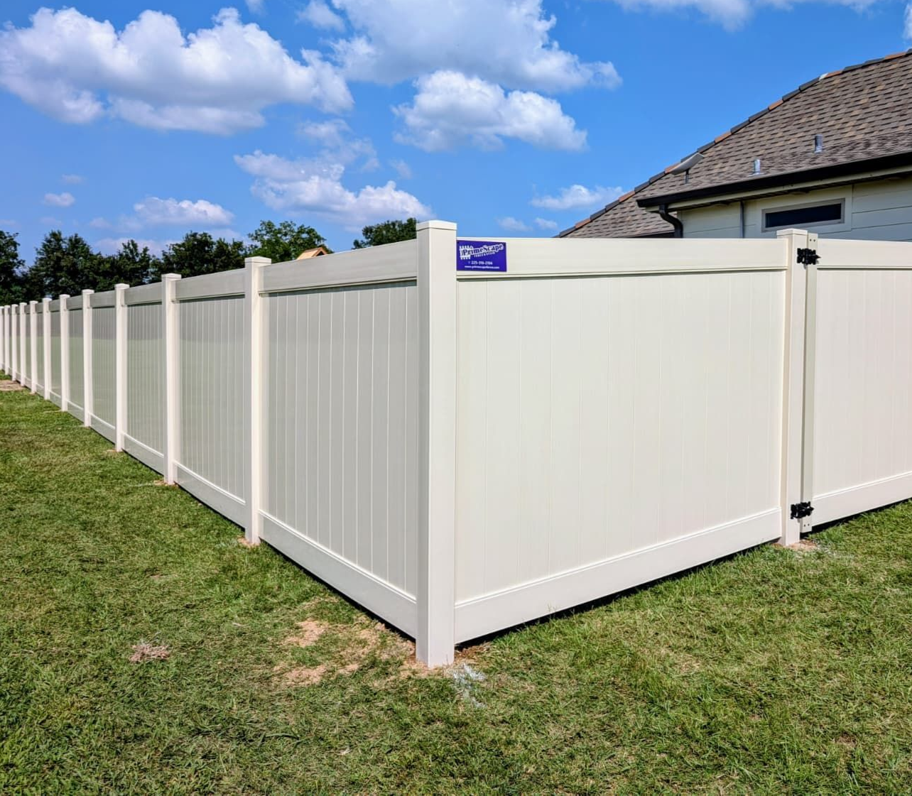 White vinyl privacy fence along a grassy yard beside a house under a blue sky