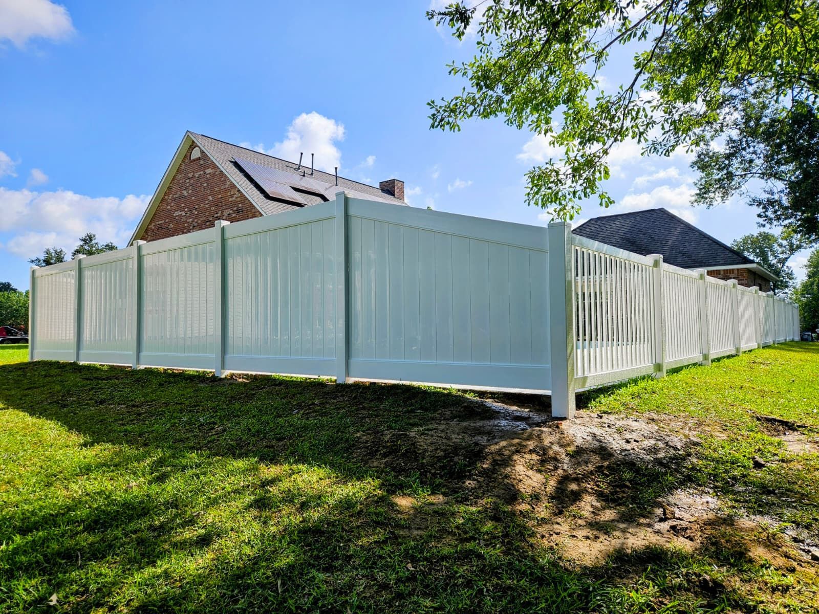 White vinyl privacy fence around a yard beside brick houses under a blue sky