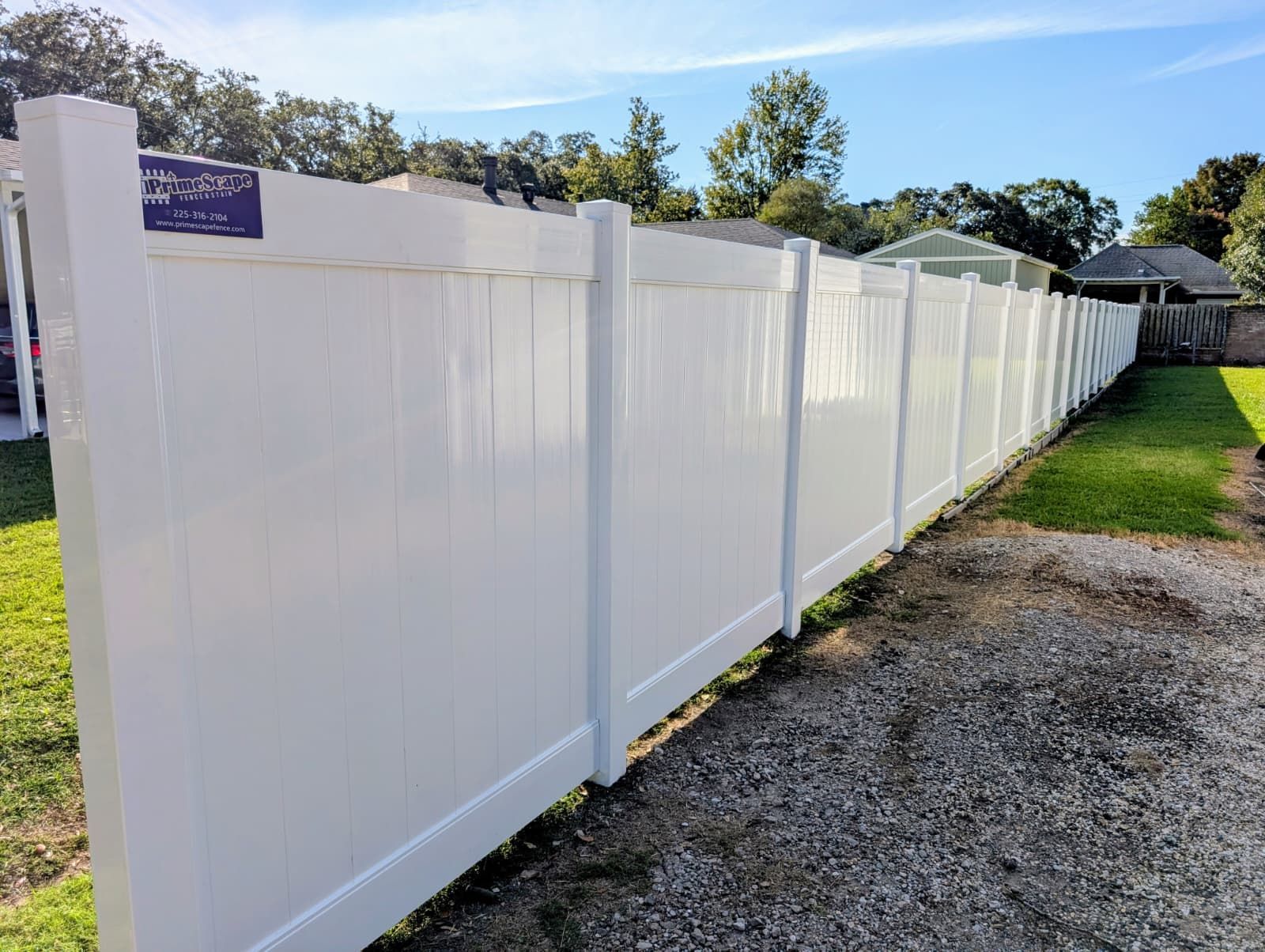 White vinyl fence beside a gravel path and grassy yard under a blue sky