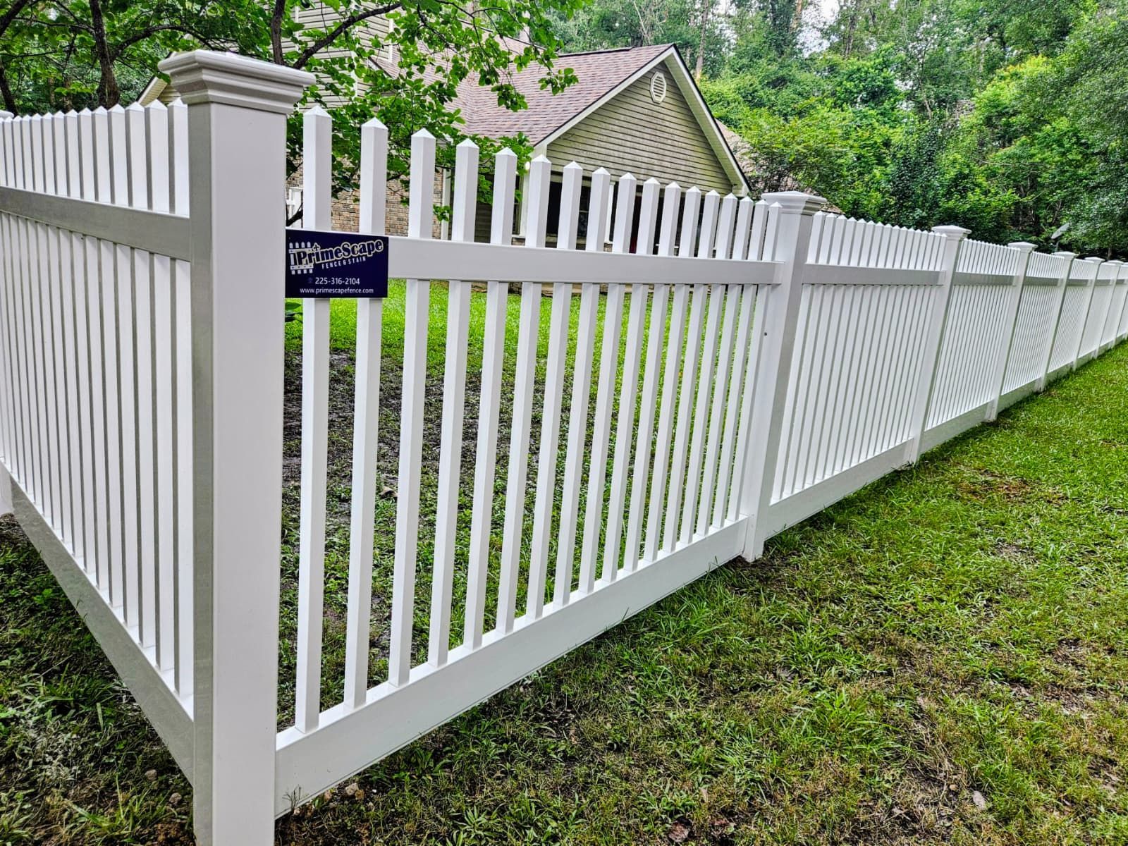 White picket fence with a gate along a grassy yard beside a house and trees