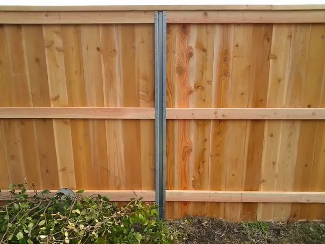 Wooden privacy fence with a gray metal post and bushes at the bottom