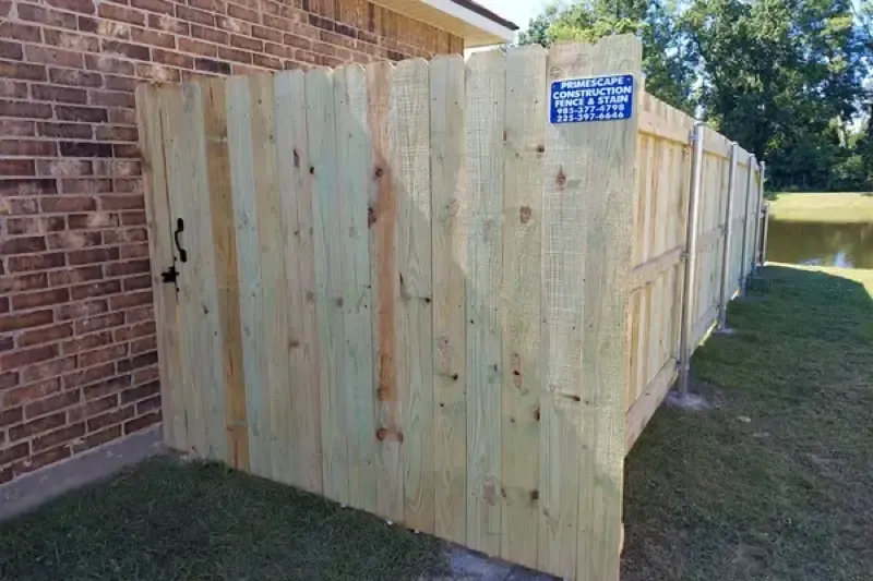 Wooden privacy fence beside a brick house along a grassy yard, with a blue sign on the fence.