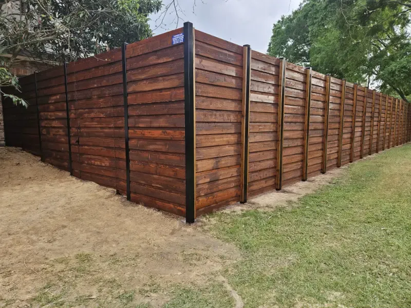 Wooden privacy fence with black posts enclosing a yard beside grass and trees