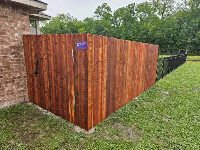 Wooden privacy fence enclosing a corner yard beside a brick house and black chain-link fence.