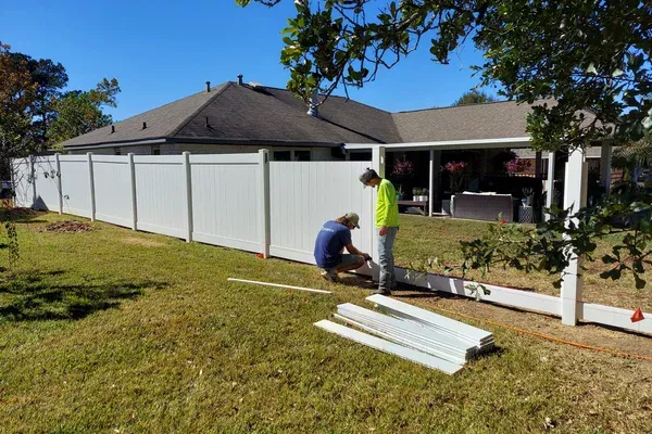 Workers installing a white fence beside a house on a sunny day