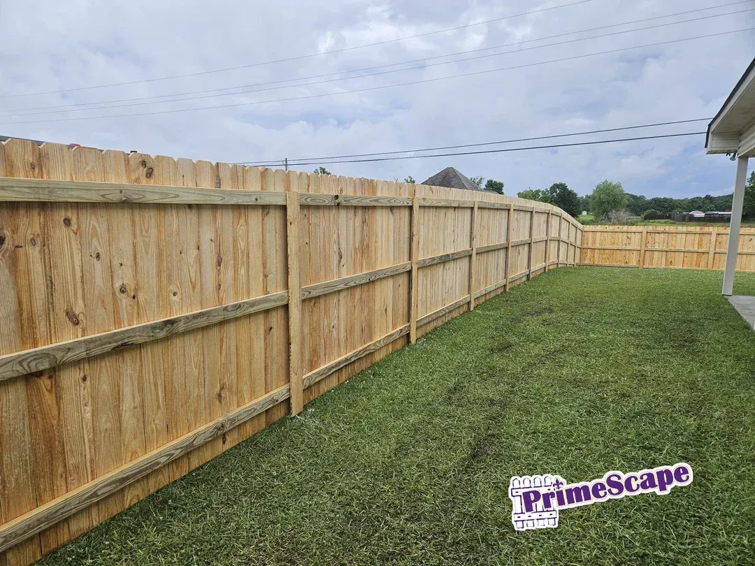 Wooden privacy fence beside a grassy yard under a cloudy sky, with a house on the right.