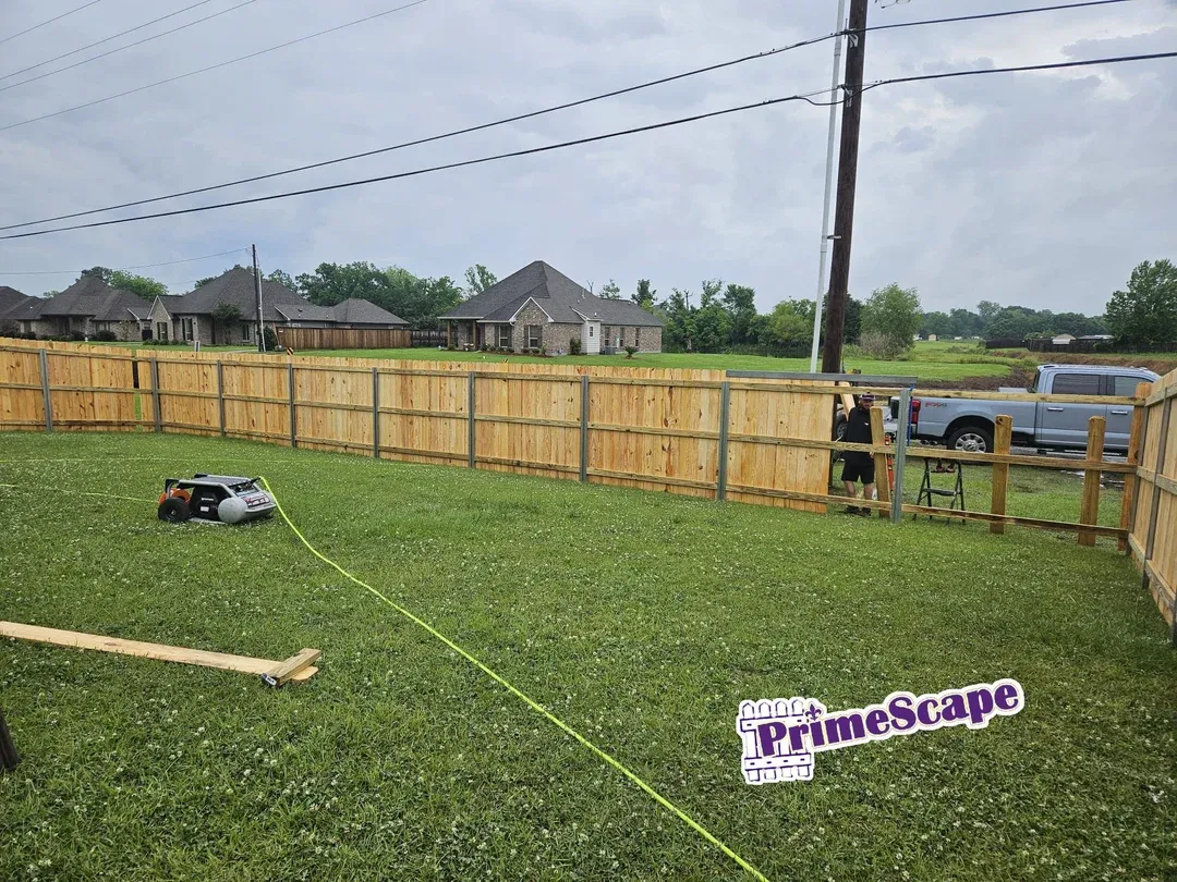 Newly fenced backyard with green grass, a utility vehicle, and a fallen Primescape sign near a power pole