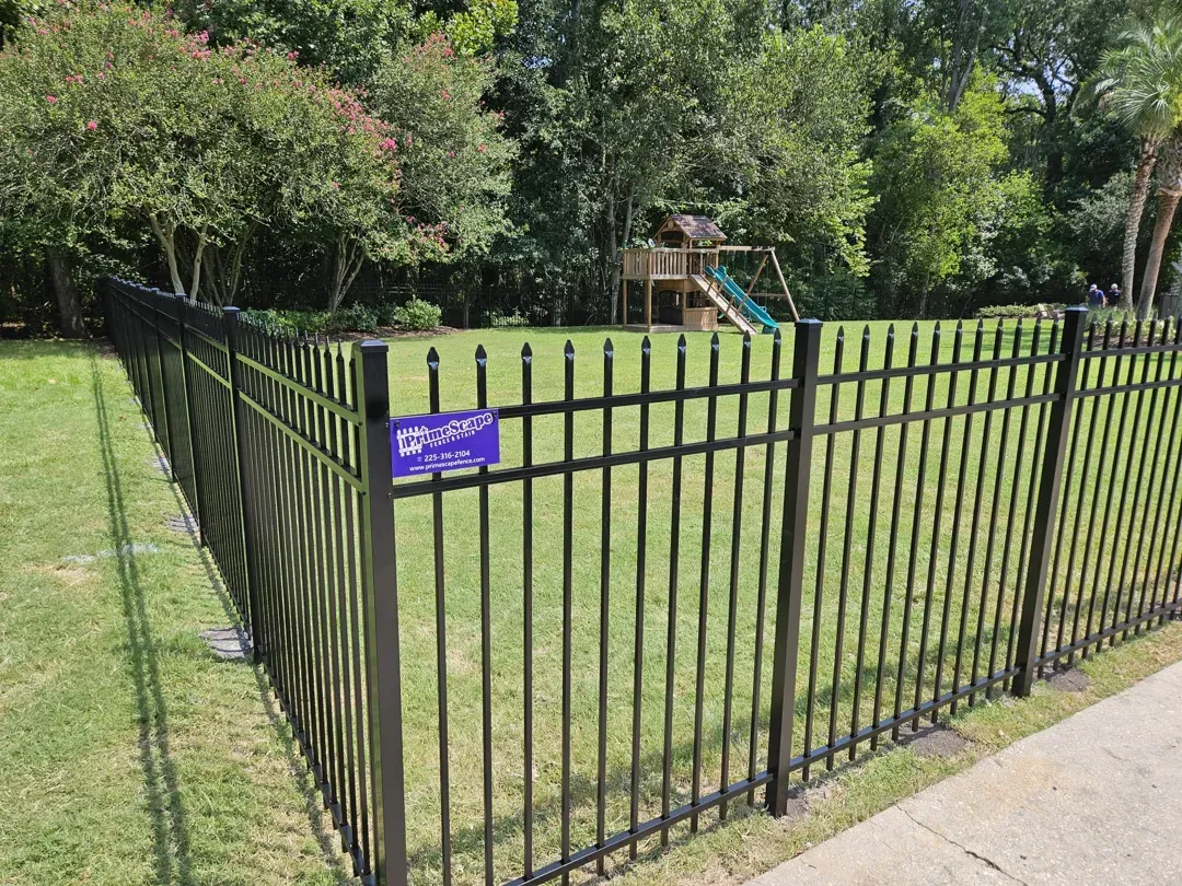 Black metal fence around grassy yard with trees and a small sign near a sidewalk