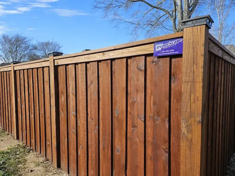 Wooden privacy fence with a purple sign on the corner, outdoors on a sunny day.