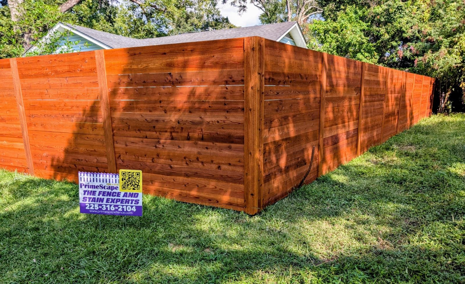 Wooden privacy fence paneling on a grassy yard, with a small sign at the corner.
