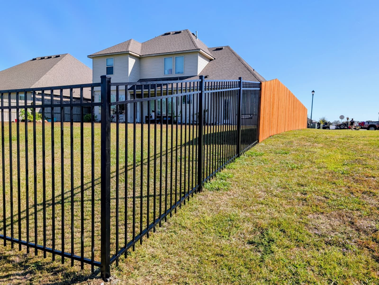 Black metal fence along a grassy slope beside a suburban house with a wooden privacy screen.