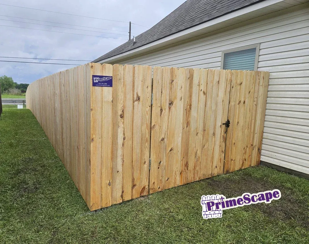 Wooden privacy fence beside a white house with a small gate, on a grassy yard.