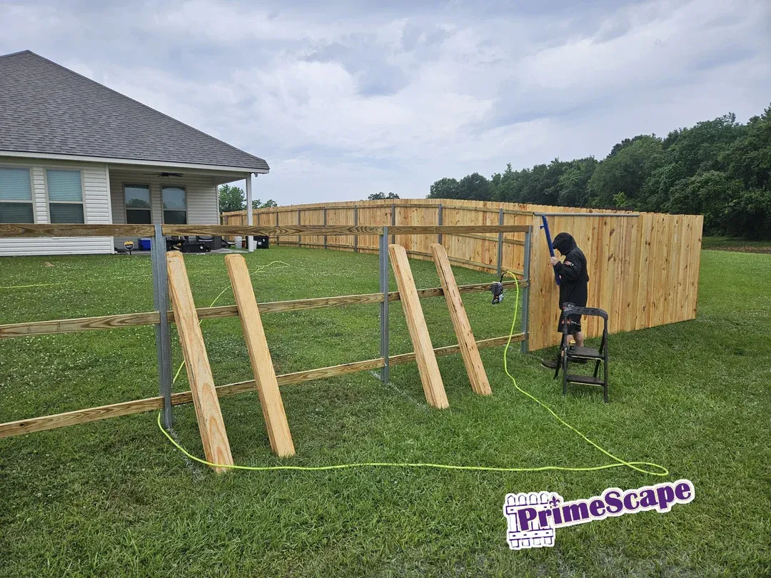 Person assembling a wooden fence in a grassy backyard beside a house