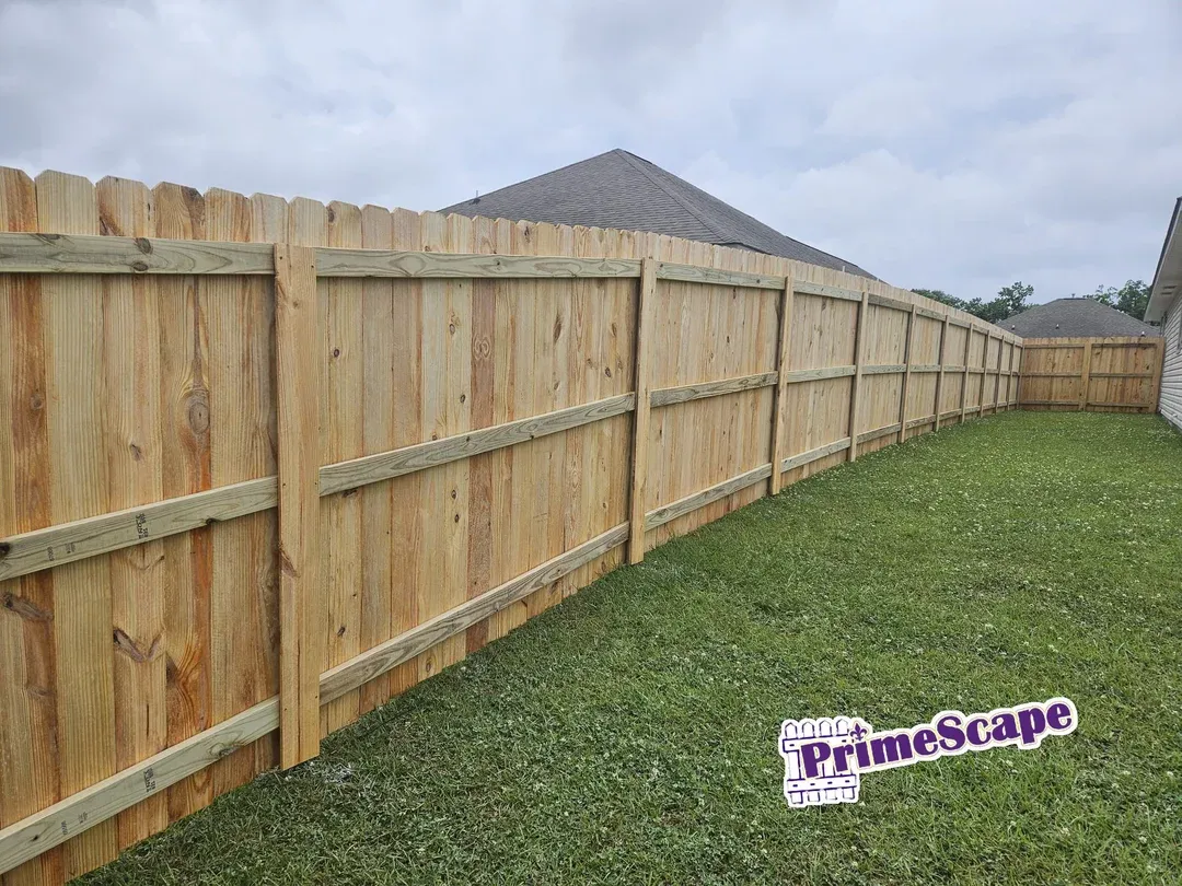 Wooden privacy fence along a grassy yard under a cloudy sky, with a PrimeScape sign in the foreground.
