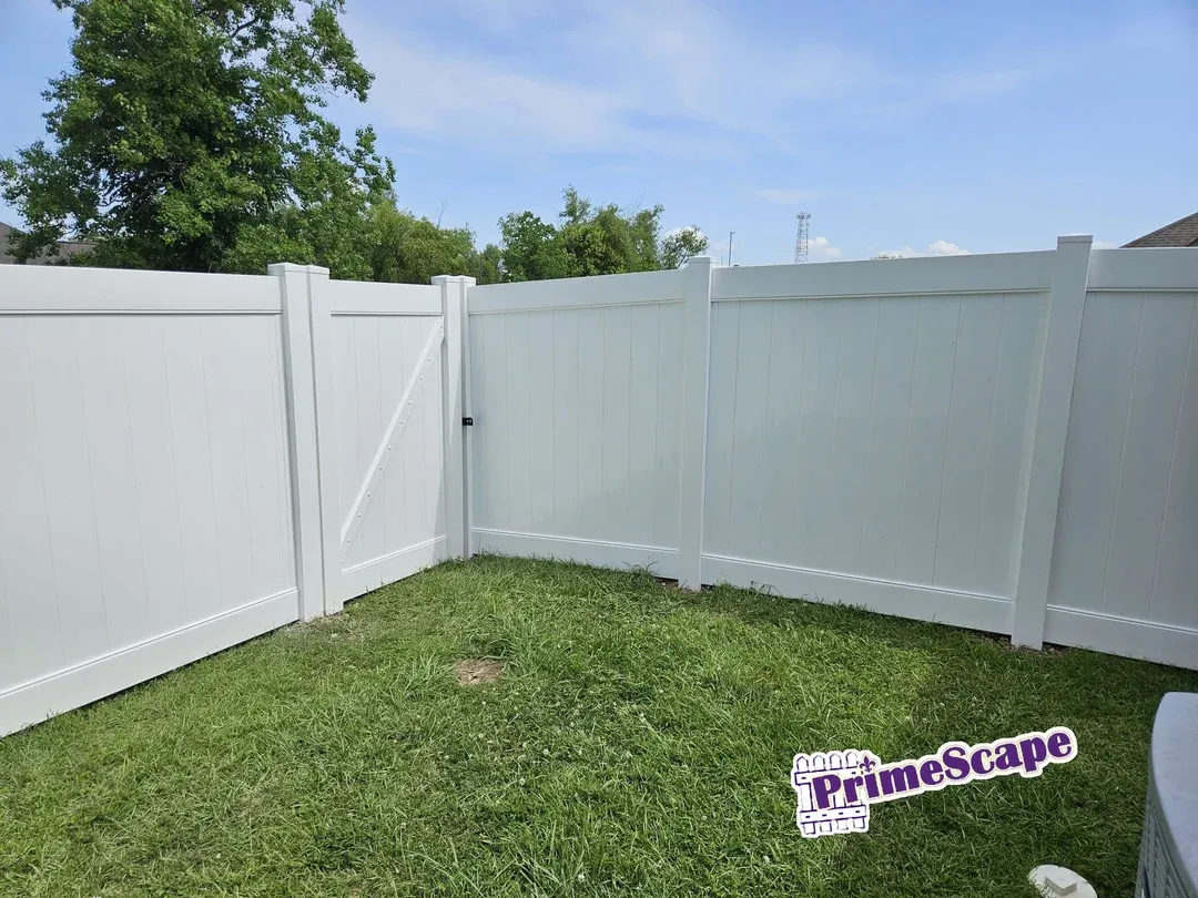 White vinyl privacy fence enclosing a grassy backyard with a gate and blue sky above