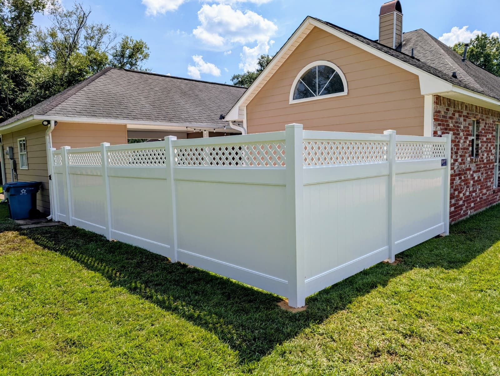 White vinyl privacy fence around a suburban backyard beside a tan house under a sunny sky