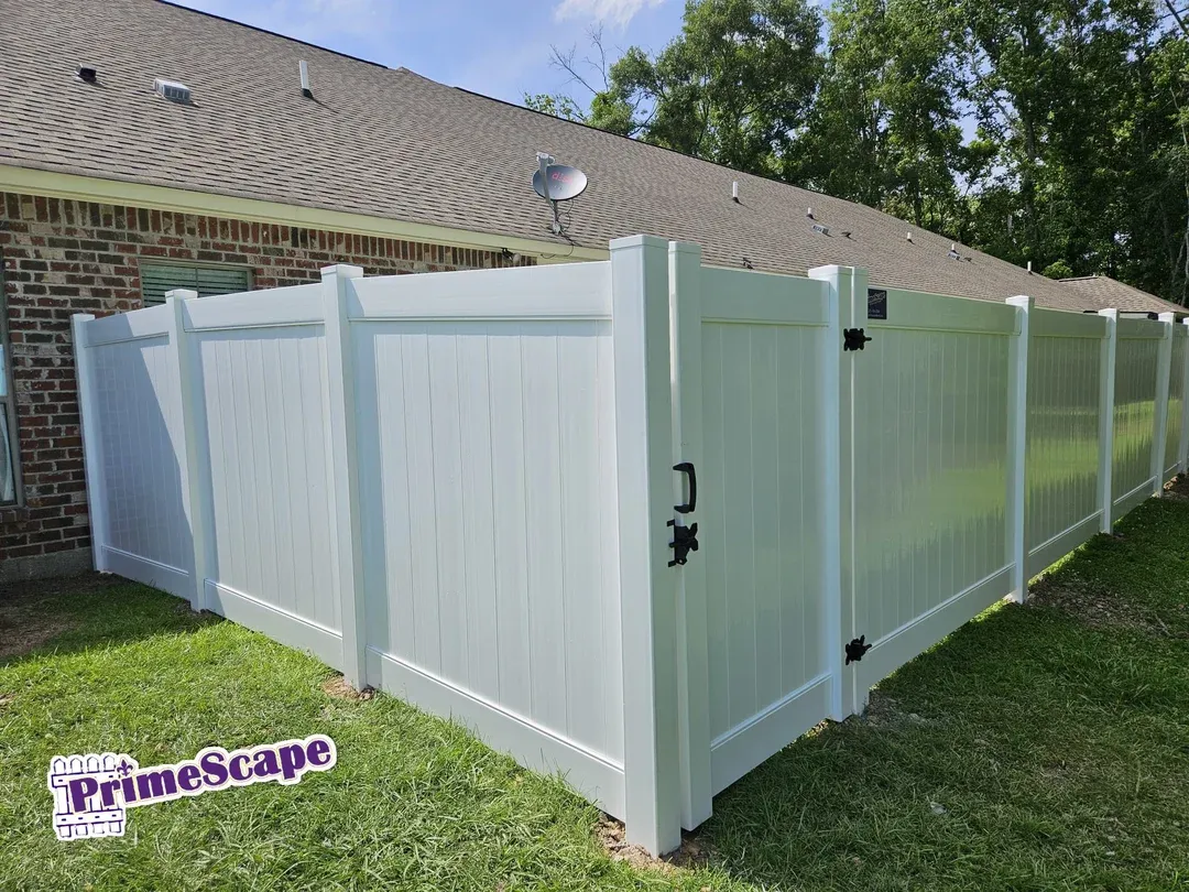 White vinyl fence panels with gates enclosing a backyard beside a brick house.