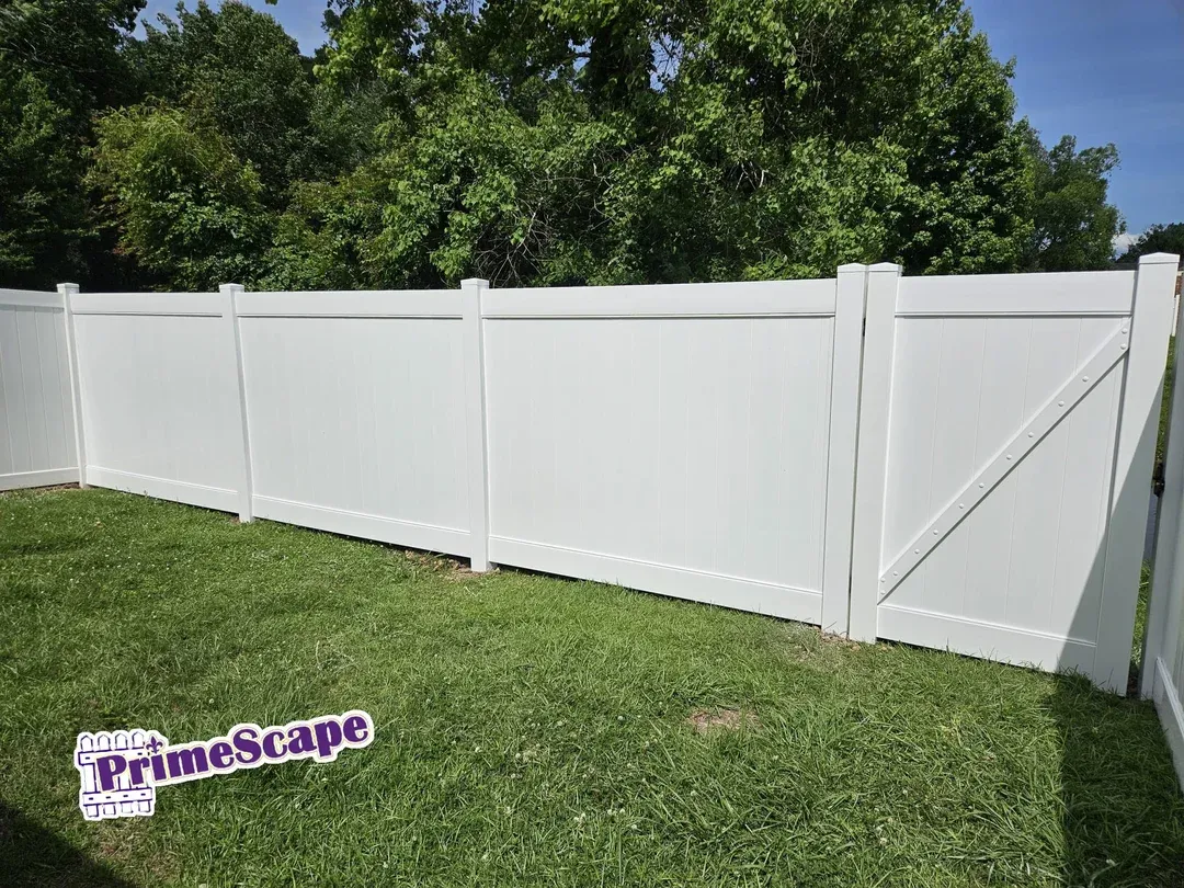 White vinyl privacy fence with diagonal brace in a grassy yard, backed by tall green trees.
