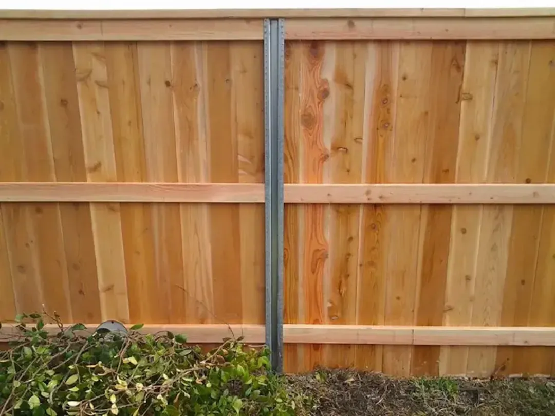 Wooden privacy fence with a gray metal post and shrubs along the bottom edge.
