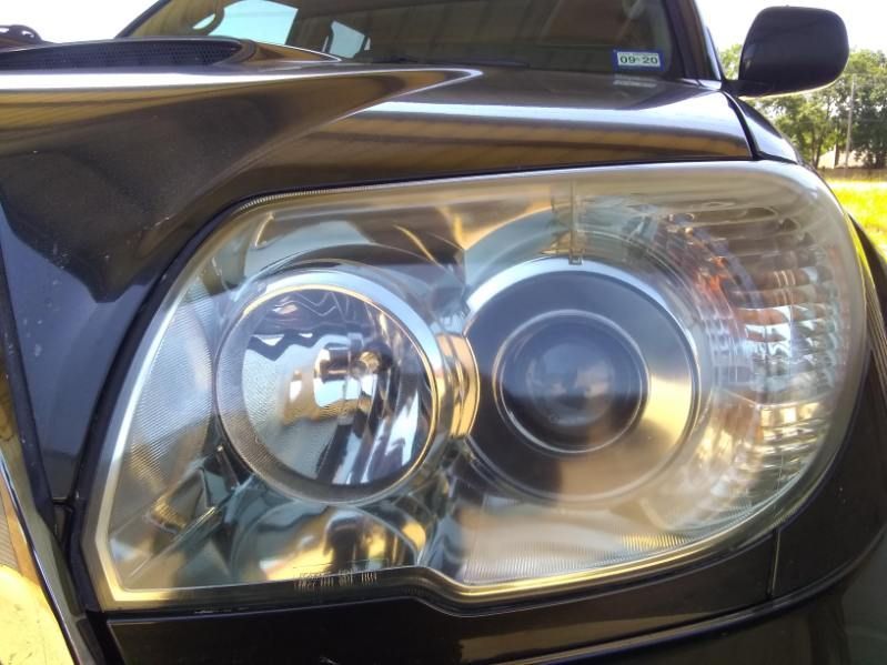 Close-up of a black car’s front headlight and chrome grille, with sunlight reflecting off the lens.