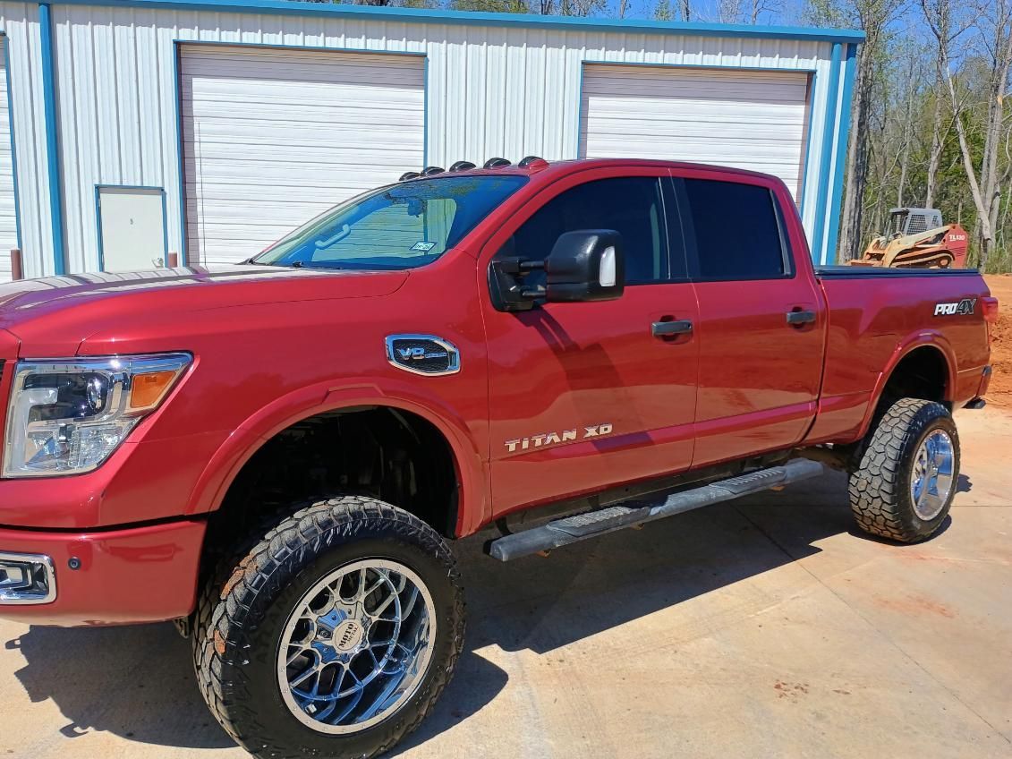 Red lifted pickup truck parked outside a garage with blue trim and white roll-up doors.