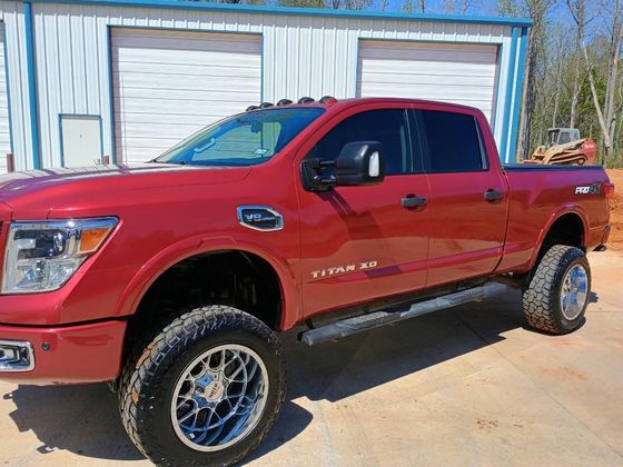 Red lifted pickup truck parked outside a garage with blue trim and white roll-up doors.