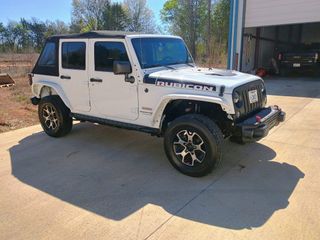 White Jeep Wrangler parked on a driveway, with black trim and off-road wheels, near a garage.