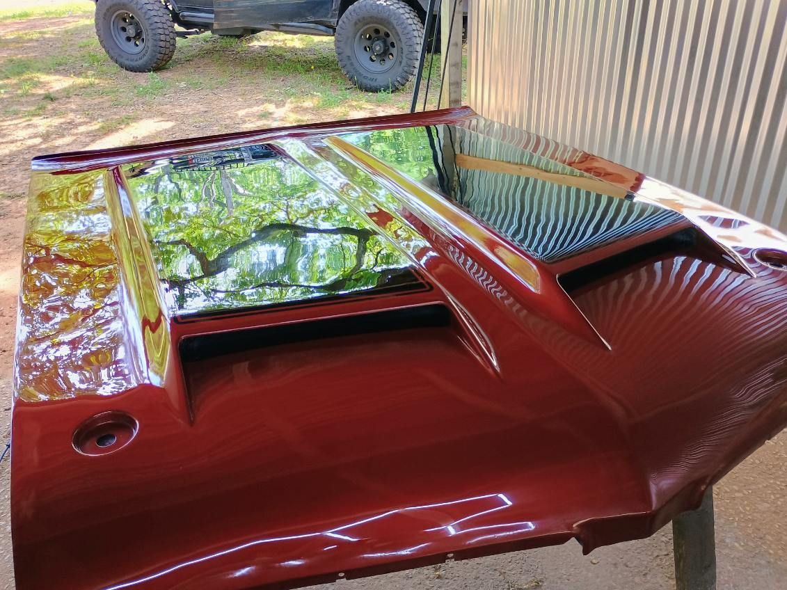 Red car body panel with tinted rear glass, parked outdoors near a corrugated wall.