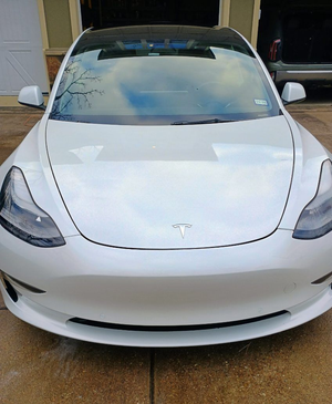 White Tesla sedan parked in a driveway, front view.