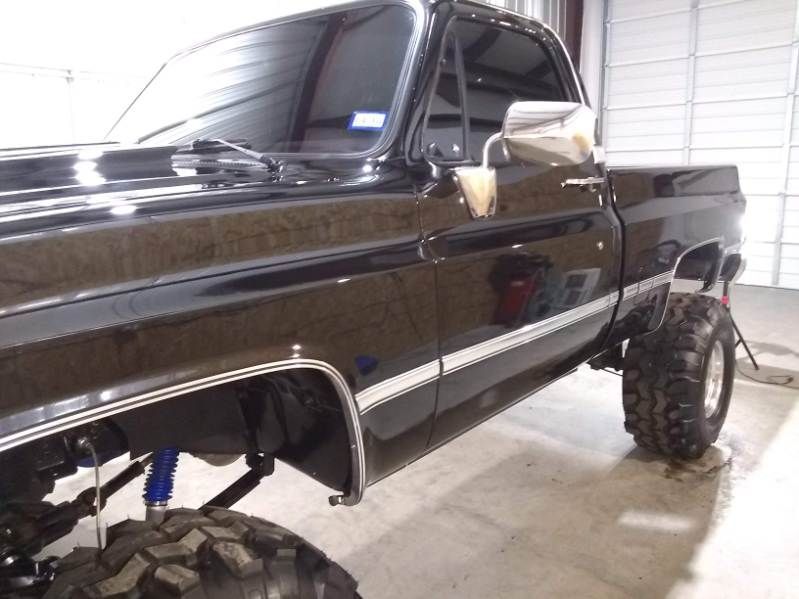 Black pickup truck with oversized rear off-road tires in a garage or workshop
