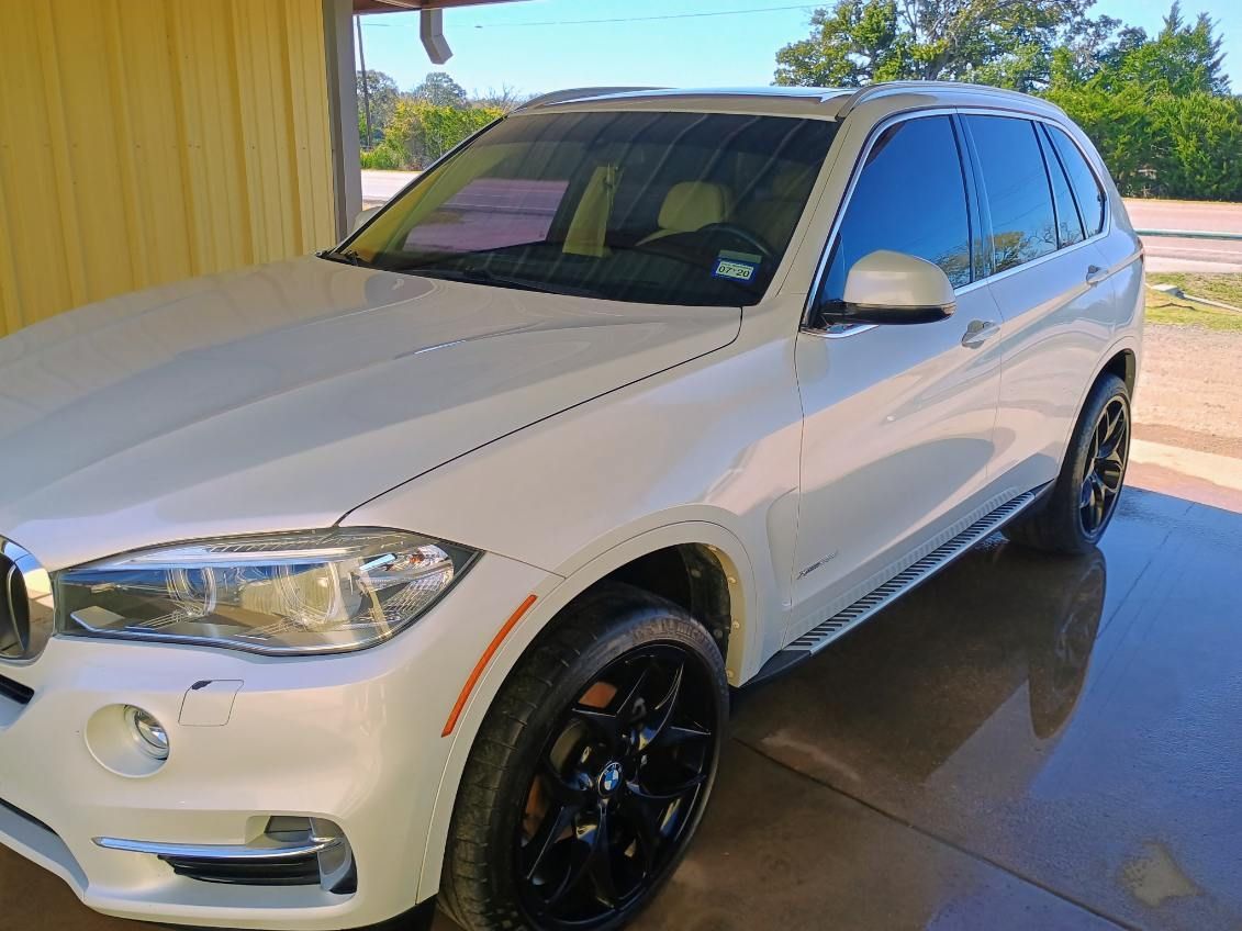 White BMW SUV parked by a yellow wall on a sunny driveway, with black wheels and tinted windows