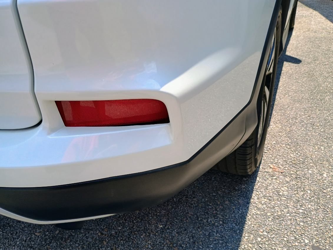 Close-up of a white car’s rear bumper and red taillight on pavement