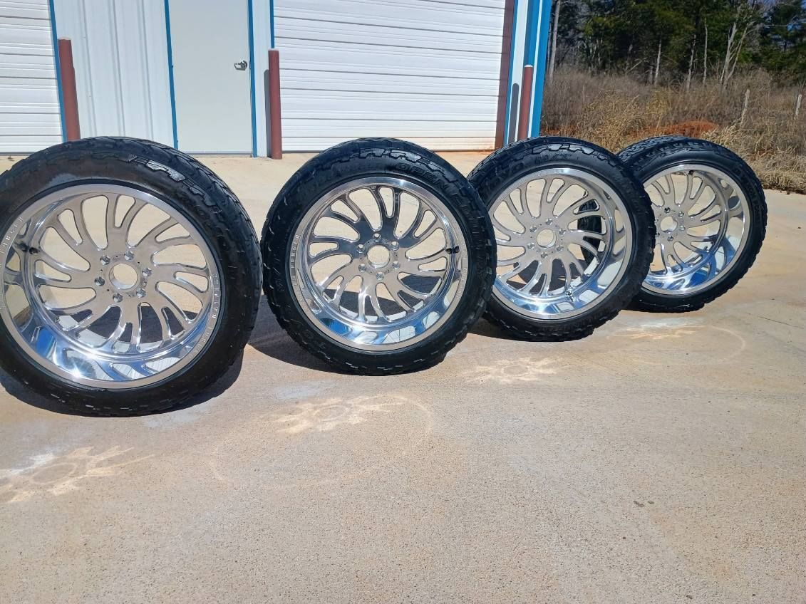 Four chrome car rims with black tires lined up on a concrete surface outside a building.