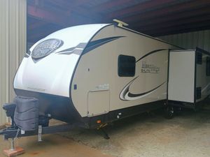 White and beige travel trailer parked under a covered carport, with a front hitch and decorative graphics.