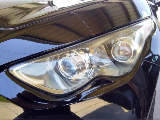 Close-up of a black car’s headlight and front hood in daylight