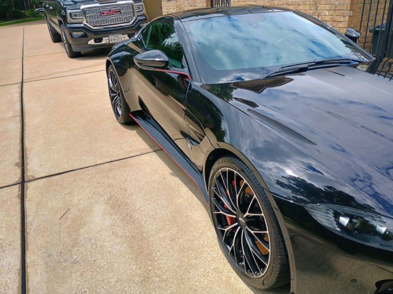 Black sports car parked in a driveway, with a gray SUV behind it.