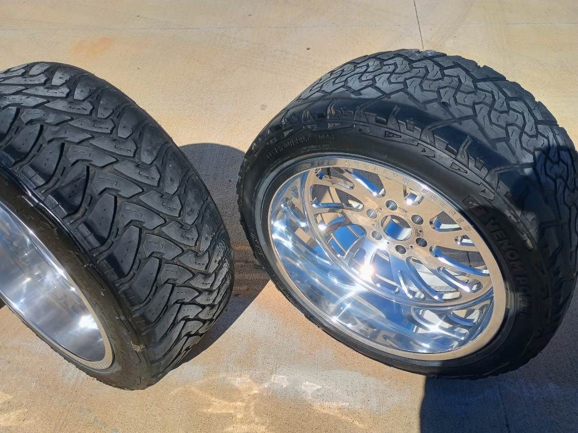 Two black off-road tires with shiny chrome rims on a concrete surface.