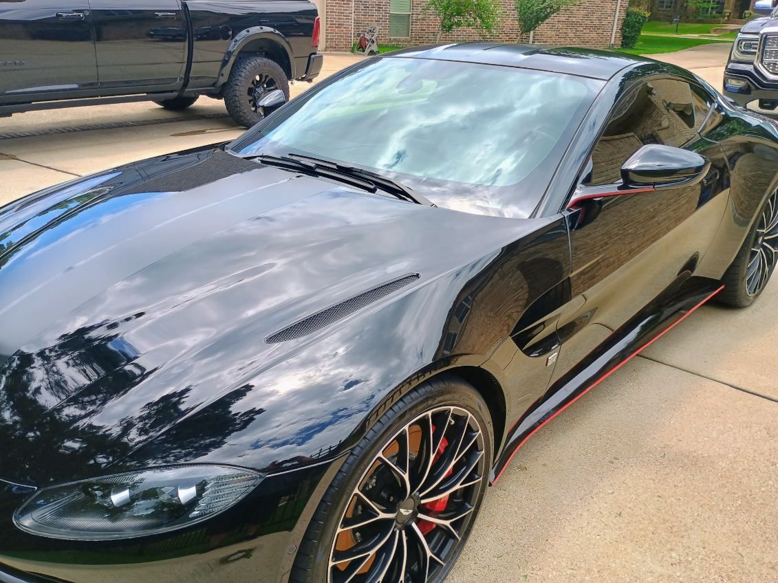 Black sports car parked in a driveway, front three-quarter view, with red-accented rims.