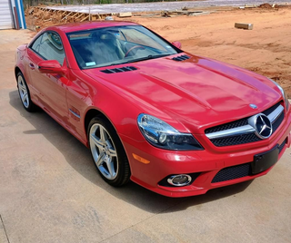 Red Mercedes-Benz coupe parked on a sandy roadside under bright sunlight