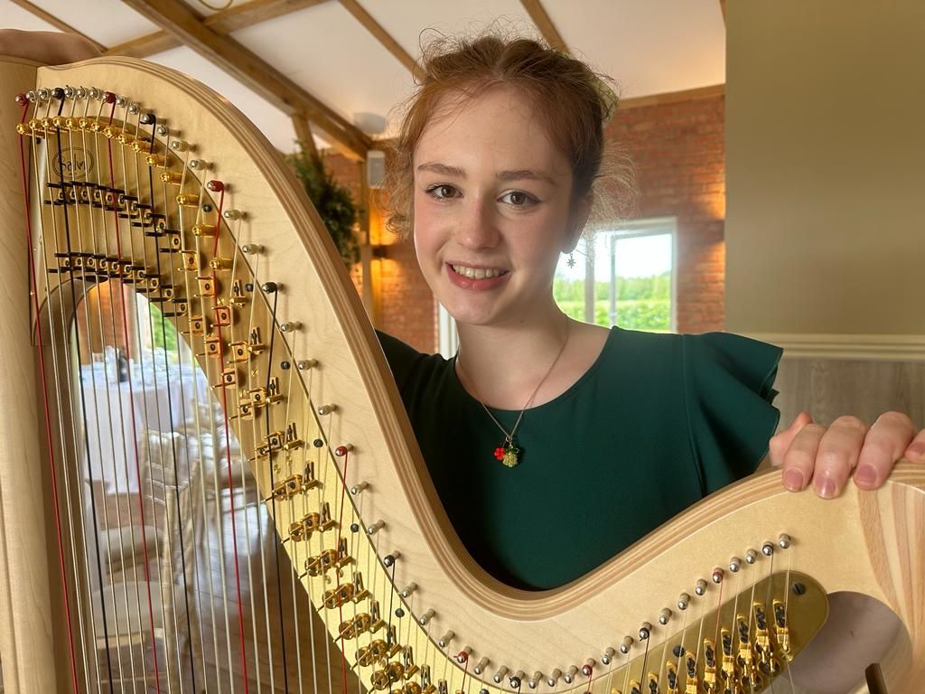 Woman smiling beside a large harp in a bright indoor room