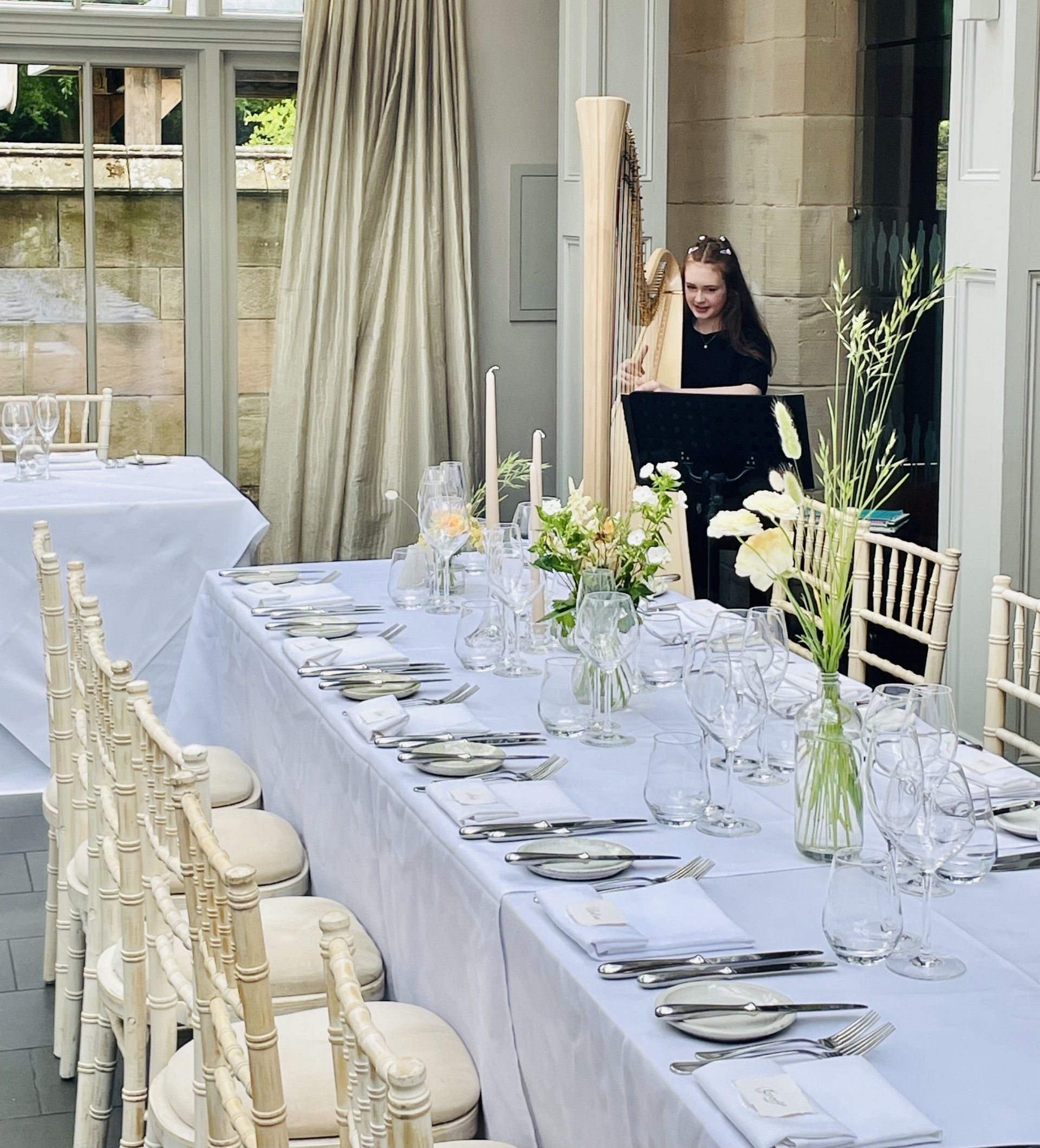 Elegant outdoor dining setup with white tablecloths, floral centerpieces, and a woman standing near a doorway